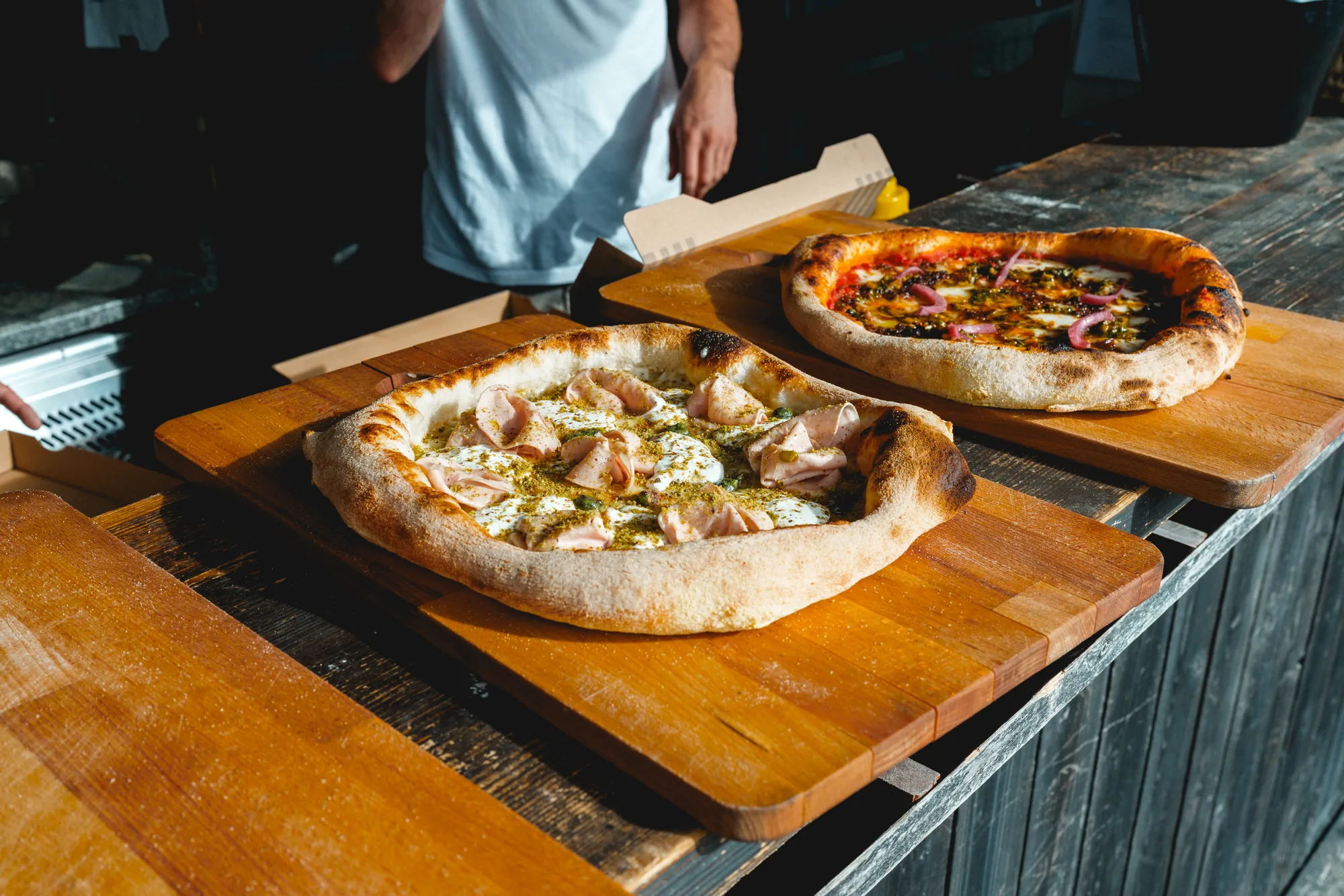 Deux pizzas sortant du four, posées sur le comptoir en bois